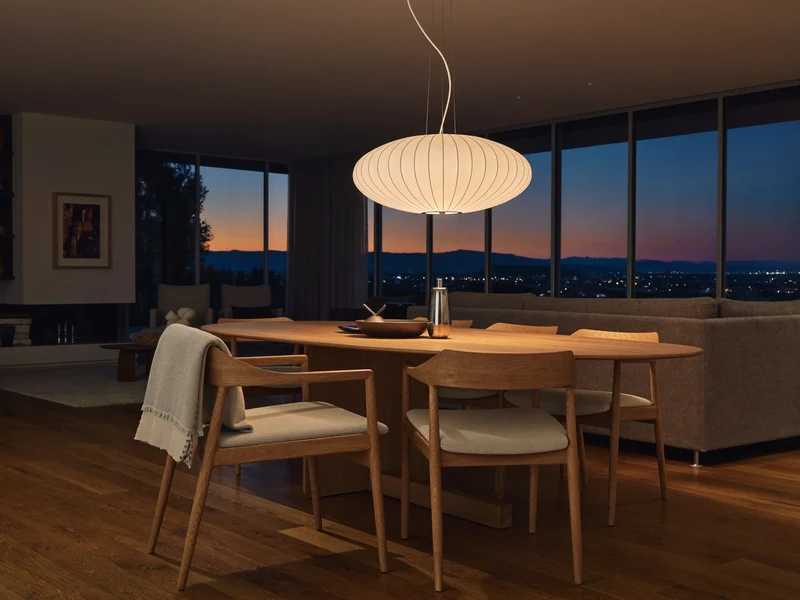 Wohnzimmer in der Dämmerung mit leuchtender Pendelleuchte über einem Esstisch